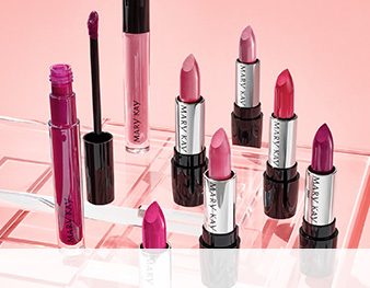 A group of red and pink Mary Kay® lipsticks and lip glosses photographed atop clear plexiglass squares in front of a pink background