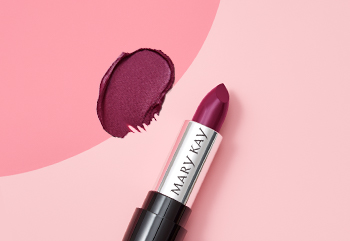 Fotografía de un lápiz labial Mary Kay® color cereza sin tapa junto a una muestra del producto sobre un fondo rosa de dos tonos.