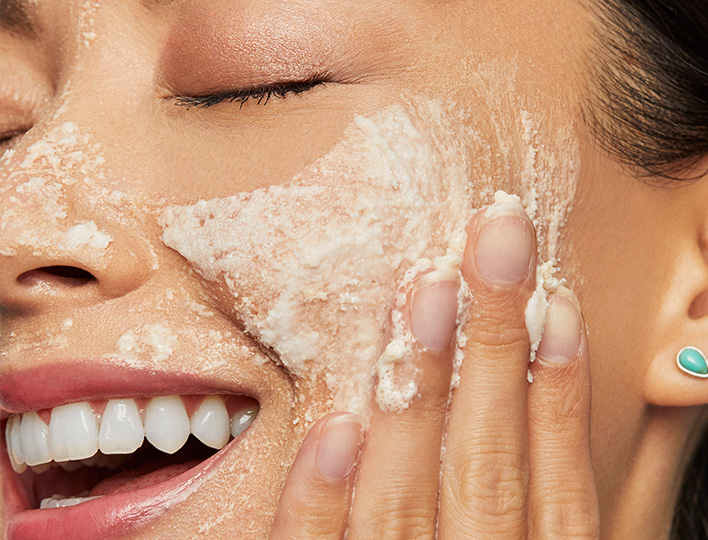 An Asian woman smiling and exfoliating with Mary Kay Naturally® Exfoliating Powder